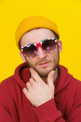 Portrait of a young handsome caucasian man in casual wear, sunglasses looking at camera on yellow background. Stylish bearded smart hipster man casual look. Thoughtful guy on yellow background