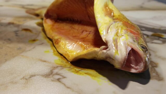 Applying the marinade with a silicone brush on fresh peeled trout. Marinade of spices and olive oil. Preparation of fish for baking.