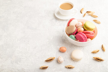 Different colors macaroons and chocolate eggs in ceramic bowl, cup of coffee on gray concrete background. side view, copy space.