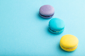 Yellow, purple and blue macaroons on blue pastel background. side view, copy space.