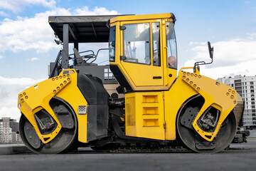 Asphalt paving machine and heavy vibratory roller close-up. A paver finisher, asphalt finisher or paving machine placing a layer of asphalt. Repaving the road surface. Road works.