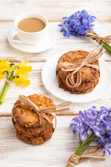 Obraz na płótnie Canvas Oatmeal cookies with spring snowdrop flowers bluebells, narcissus and cup of coffee on white wooden background. side view, close up.