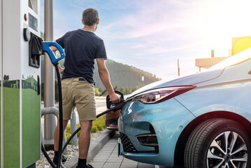 Naklejka premium Man powering his electric car on a charger in a public parking lot.