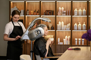 young woman under hooded dryer machine in hair salon
