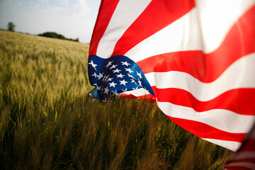 4th of July. USA flag against beautiful wheat field landmark on sunset