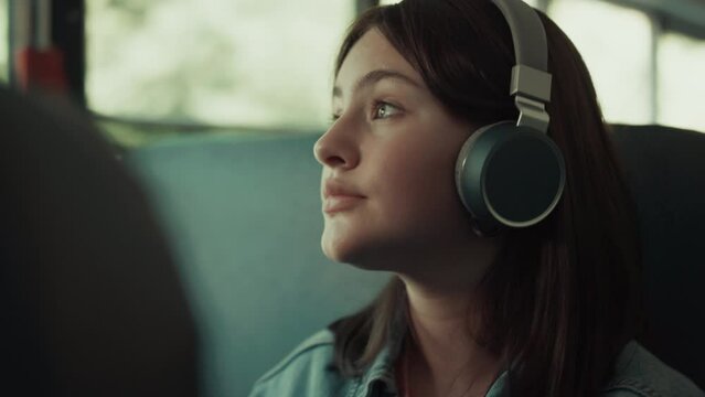 Girl teenager traveling bus with headphones close up. Brunette listening music.