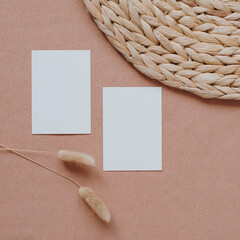 Paper sheet cards with blank copy space for branding. Invitation cards mockup template, dried grass stalks, straw napkin on pastel coral pink table background. Aesthetic luxury invitation, brand cards