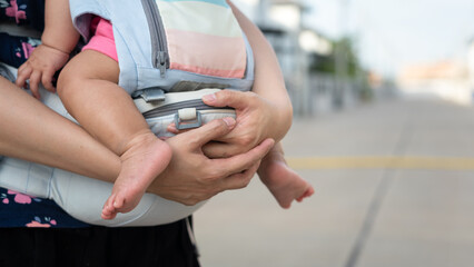 A mother is holding the baby by using baby carriage strap belt. Parenthood action scene photo. Selective focus.