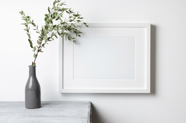 Blank landscape frame mockup with eucalyptus twig over white wall