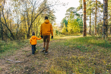 Father and son walking in autumn forest.