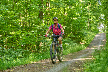 Naklejka premium nice active senior woman riding her electric mountain bike in the green city forest of Stuttgart, Germany