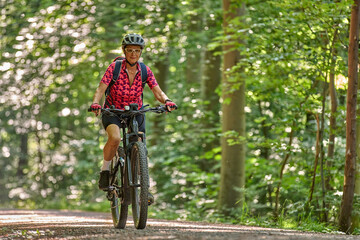 Naklejka premium nice active senior woman riding her electric mountain bike in the green city forest of Stuttgart, Germany