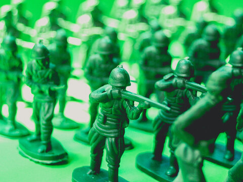 Small toy soldiers of green color in battle in front of green background.