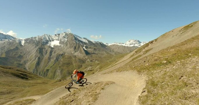Cruising on a enduro mountainbike down a sigle trail with fun curves and amazing panorama landscape view in high alpine terrain. Colerful sportswear and great sunlight on a sunny spring day. 4K 30fps.
