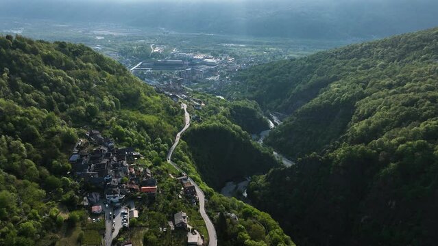 Flight above road through idyllic Italian village in alp valley hillside; drone