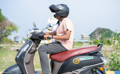 Man driving Ev or electric scooter by wearing helmet on road - concept of safety, technology and lifestyle. © WESTOCK