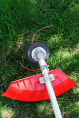 Reel of gas trimmer with fishing line, lawn mower on grass background. Trimmer head