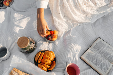 Fruits and book on white blanket, picnic outdoor.