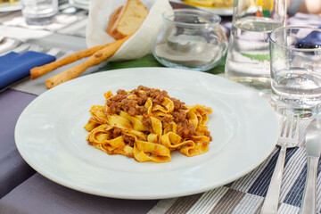Italian Dinner in restaurant. Tagliatelle all ragu bolognese, traditional type of pasta from the Emilia-Romagna region of Italy.  Served with classic  meat sauce or Bolognese sauce. Lifestyle photo. © Olga