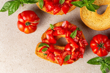 Friselle or frese, a type of twice-baked bagel shaped bread from Puglia, Italy. Briefly soaked in water first, and topped with summer tomatoes, basil and olive oil. Italian summer food concept.
