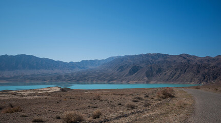 Fototapeta na wymiar Lake with mountains on the background. Mountain range view. A sultry haze over desert mountains and a salty turquoise lake.
