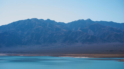 Lake with mountains on the background. Mountain range view. A sultry haze over desert mountains and a salty turquoise lake.