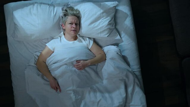 Annoyed woman can't sleep because of noise from neighbors while lying in bed in bedroom, top view.