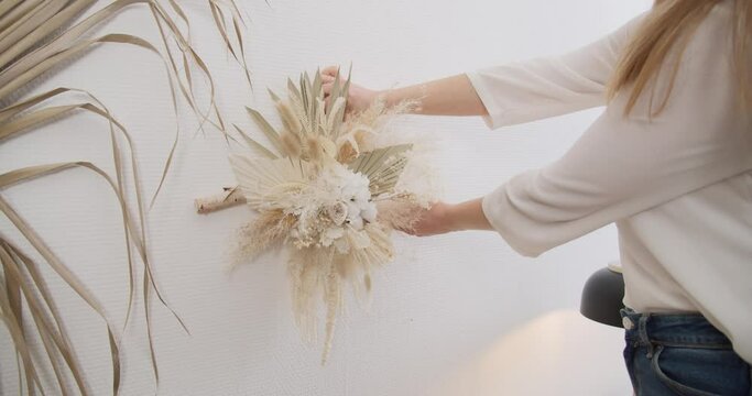 Stunning bunch of white, ivory and beige dried flowers being put as a wall hanging by female florist. 