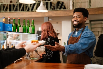 Black bearded man wearing apron smiling while working in cafe
