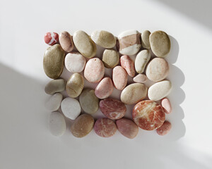 Plakat Creative arrangement of natural colored sea stones with sun shadow. Smooth round pebbles as square pattern on light background. Minimal summer flat lay, top view still life composition