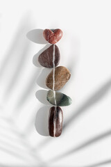Top view still life sea stones, pebbles united by one vertical row with heart stone above with palm leaf shadow. Natural rocks natural tones. Summer Minimal flat lay, love and romance concept