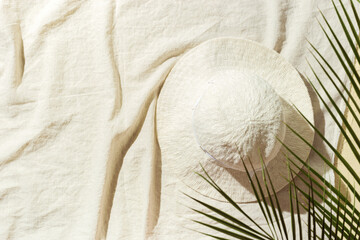 Summer lifestyle background, top view wide-brimmed sun hat under green palm leaves on beach towel...