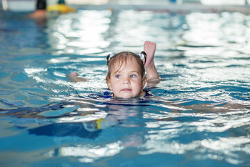 Fototapeta na wymiar Small preschooler kid learns to swim with board in pool. Swimming lesson. Active kid plays in water