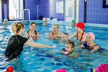 Group of mothers with little babies in children's swimming section with coach. Healthy lifestyle.