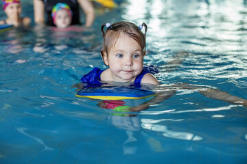 Fototapeta na wymiar Small toddler kid learns to swim with board in pool. Swimming lesson. Active kid plays in water