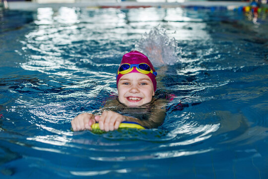 Child schoolgirl learns to swim with board in pool. Swimming lesson. Active child plays in water