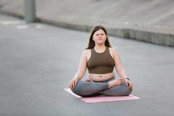 Plus size girl teenager meditates on yoga mat outside in summer, excess weight in teenagers, calmness and yoga classes