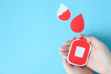 hand holding bloody bag shape made from paper on blue background, copy space, top view. blood donation concept, world blood donor day