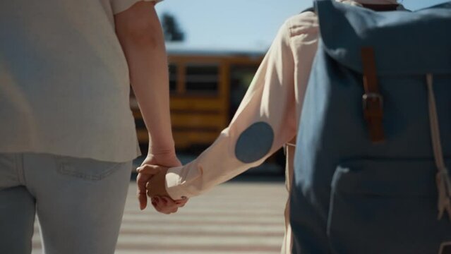 Mother holding son hand walking together to schoolbus sunny morning close up.