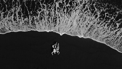 Couple lie on a black sand near ocean - Powered by Adobe