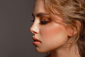 Fototapeta premium Beauty young girl in profile with perfect smooth skin and makeup with wavy hair looks away on a gray background, skin care, cosmetology