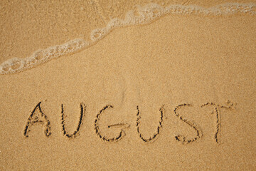 August - handwritten on the soft beach sand.