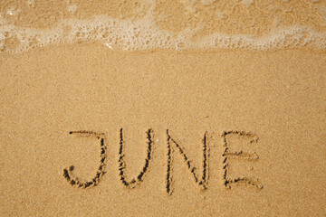 June - handwritten on the soft beach sand.