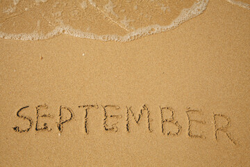 September - handwritten on the soft beach sand.