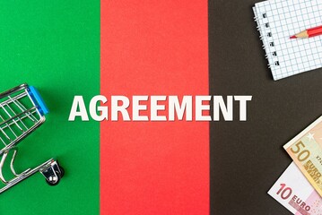 AGREEMENT - word (text) and euro money on a table of different colors, a trolley, a basket of grocery notepad and a red pencil. Business concept, buying, selling, supermarket, store (copy space).