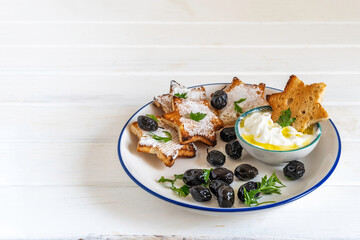 Black olives, yogurt with olive oil, sandwich with cream cheese on ceramic plate over wooden background.