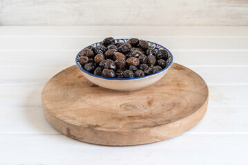 Bowl of dried black olives on wooden tray for Mediterranean snack.