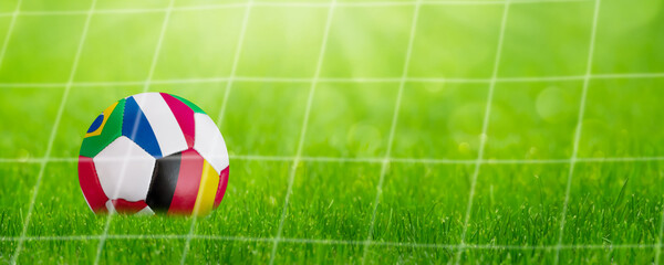 closeup of a lying colorful soccer ball in a goal behind net with international flags, symbolic...