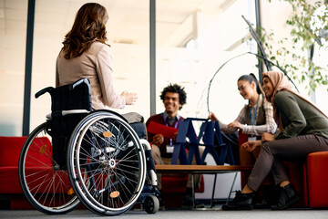 Rear view of businesswoman in wheelchair and her colleagues talk on break in the office.