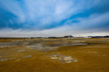Icelandic landscape looking like on the planet Mars surface with yellow ground and blue streams. Steam is coming out of bubbling pits filled with blueish sulphate substance